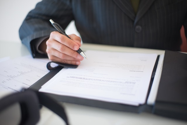 person in a blue suit holding a pen to sign a contract in front of them